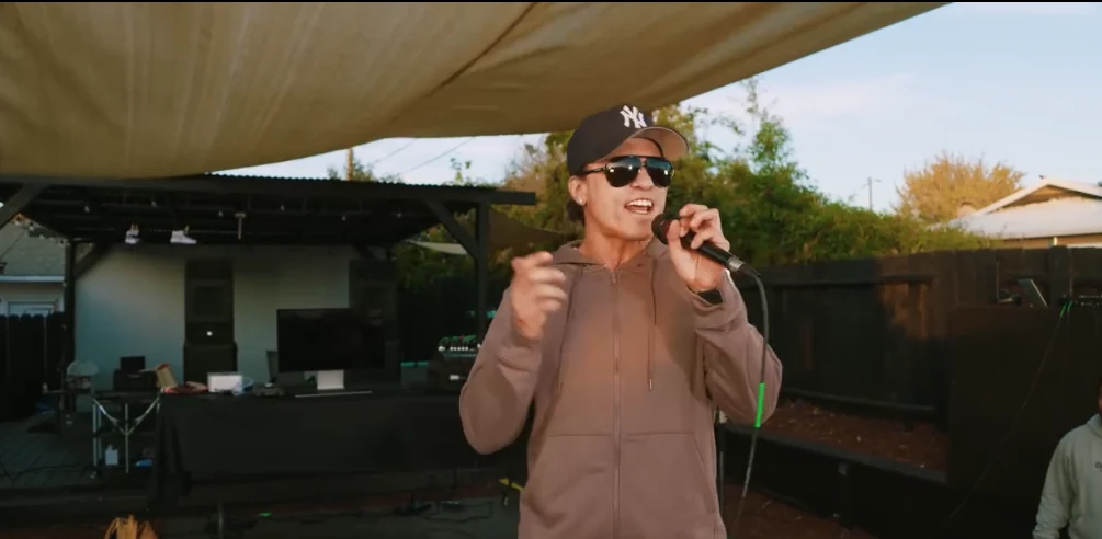 Avery Storm performing outdoors in a Yankees cap and sunglasses, singing into a microphone