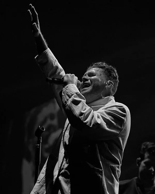 Daniel Merriweather singing into a microphone with one arm raised, in black and white