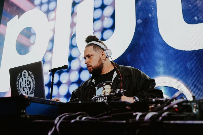 DJ Omega at the decks wearing headphones, with the DJ Omega logo on his laptop