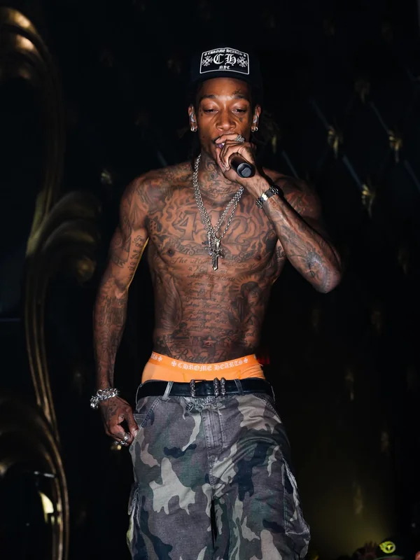 Wiz Khalifa performing on stage in a trucker hat, with a microphone to his mouth